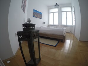 Une chambre à coucher avec un lit, une table de chevet, une lampe, une fenêtre et un radiateur.