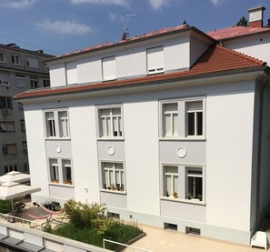 A modern building with white walls and red-tiled roof, featuring multiple windows and balconies with potted plants. - Lobagola B&B (Zagreb)