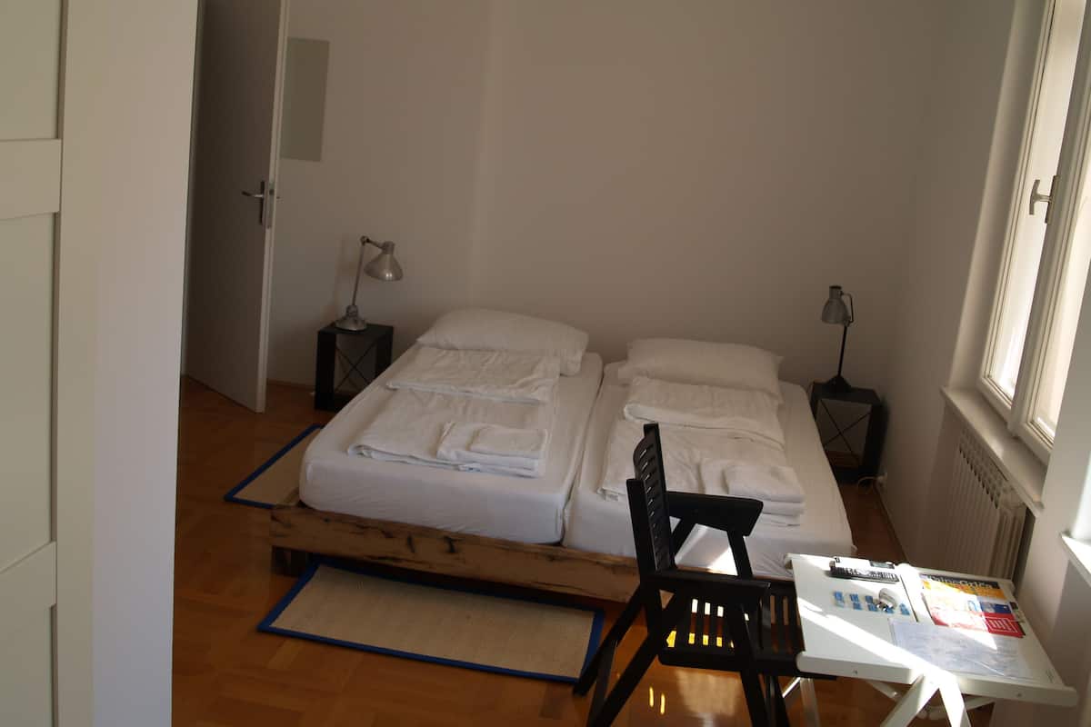 A small, clean room with a bed, a desk, and a chair. There are two bedside tables with lamps.