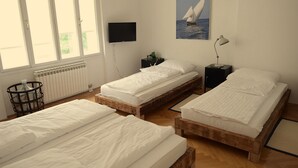 Ett rum med två sängar i trä, en tv som är monterad på väggen, ett nattduksbord med en lampa och en målning av en segelbåt på väggen.