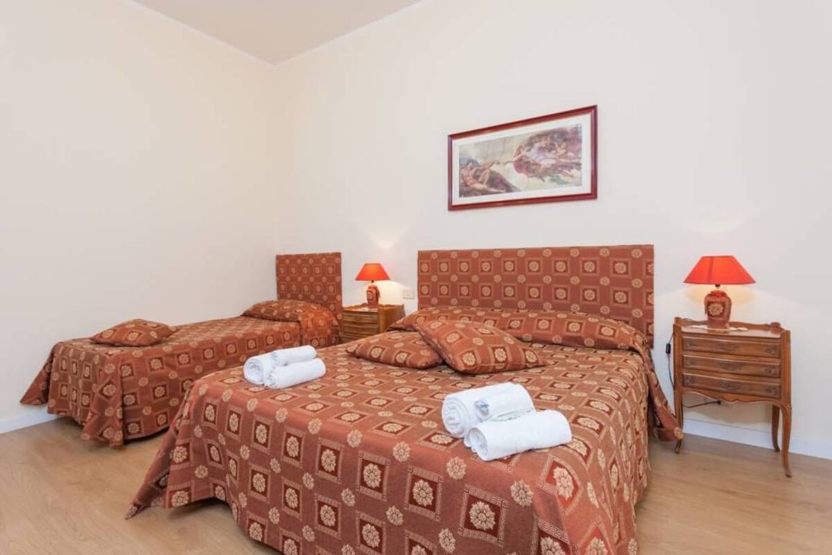 A hotel room with two beds, each with patterned bedding and matching pillows. There are bedside tables with lamps and a framed picture on the wall.