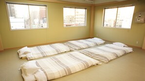 A room with two beds aligned parallel to each other, large windows, and a view of buildings outside. - Guesthouse SUN - Hostel (Osaka)