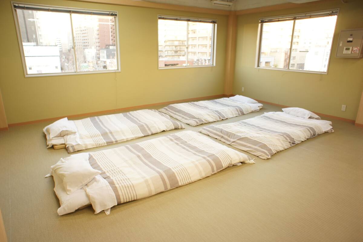 A room with two beds aligned parallel to each other, large windows, and a view of buildings outside.