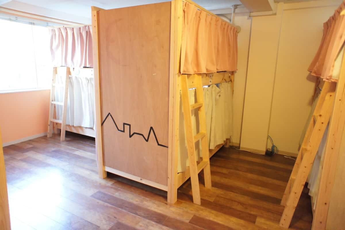 A room with a bunk bed, wooden ladder, and a window with curtains.