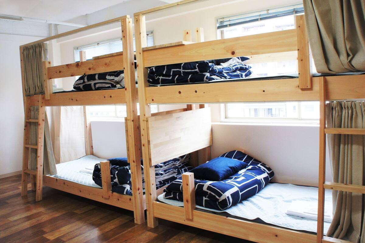 A bunk bed room with wooden frames, a window with curtains, and a wooden floor.