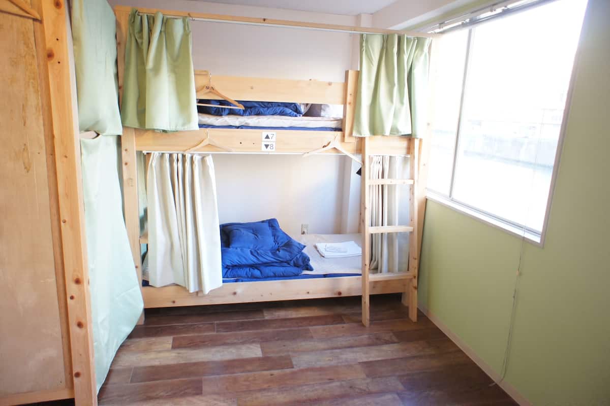 A bunk bed room with a window, wooden flooring, and curtains.