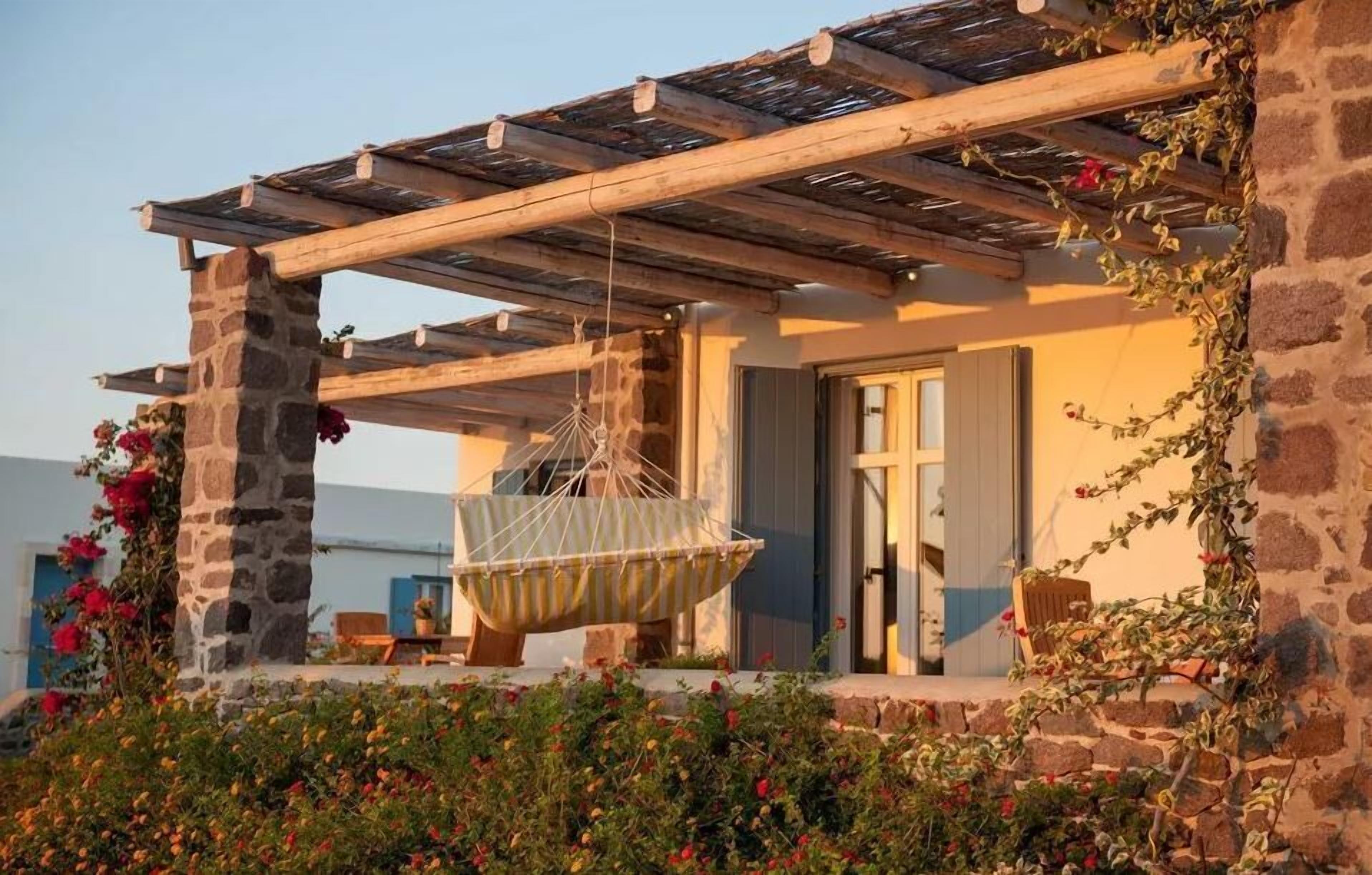 A stone building with a wooden pergola and a hanging chair.