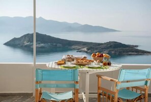 A table set with breakfast items and a view of a mountainous coastline. - Kimolia Gi Studios (Kimolos)