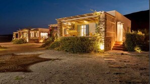 A row of modern, stone-clad houses with outdoor seating areas and a paved pathway leading to them. - Kimolia Gi Studios (Kimolos)