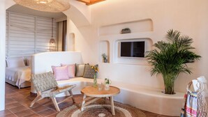A modern living room with a white sofa, a wooden coffee table, and a large potted plant. - Kimolia Gi Studios (Kimolos)