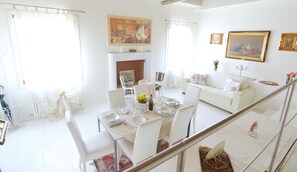 Un salón luminoso y bien iluminado con chimenea, muebles blancos y un comedor listo para una comida.