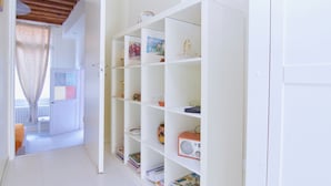 A white room with a bookshelf containing books, a radio, and decorative items. - Venezia Gentile (Venice)