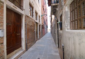 Un callejón estrecho con una puerta de madera a la izquierda y un edificio con una verja metálica a la derecha.