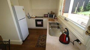 A compact kitchen with a refrigerator, oven, microwave, and sink. - Annies Garden Cottage (South Hobart)