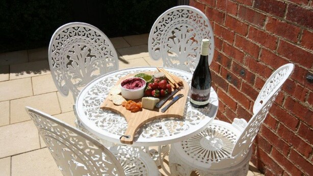 A round white table with a wooden board holding a bowl of dip, cheese, and fruit, accompanied by a bottle of wine and cutlery. - Annies Garden Cottage (South Hobart)