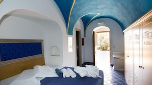 Quarto de hotel com cama, cabeceira azul, guarda-roupa e corredor que leva a um banheiro.