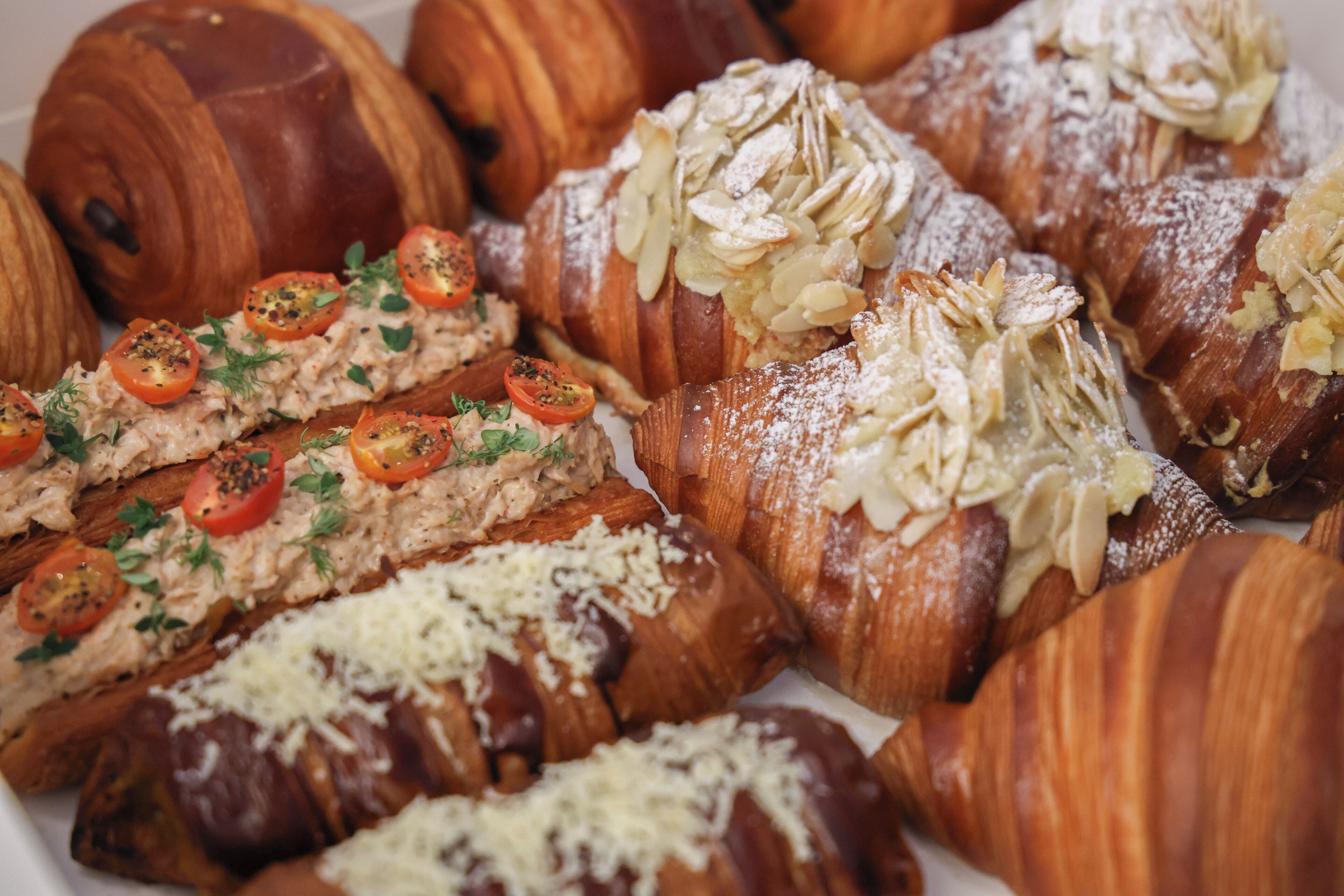 A variety of pastries including croissants and bread rolls, some topped with almonds and others with cheese and tomatoes.