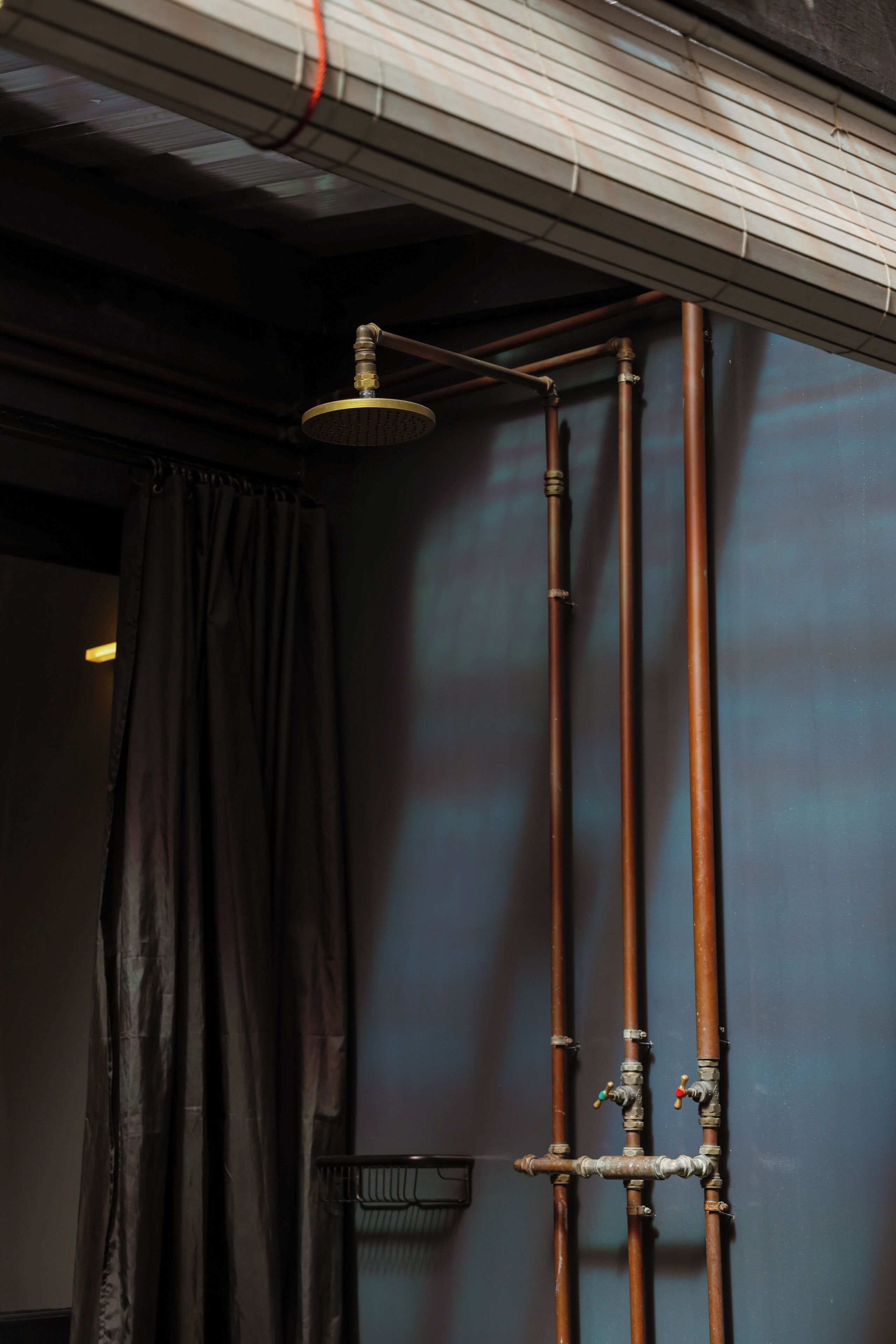 A bathroom with a shower, a curtain, and copper pipes.