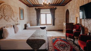 Una stanza con due letti, un lampadario grande e decorativo, un muro in pietra con decorazioni intagliate, una poltrona rossa e un televisore a schermo piatto montato a parete.