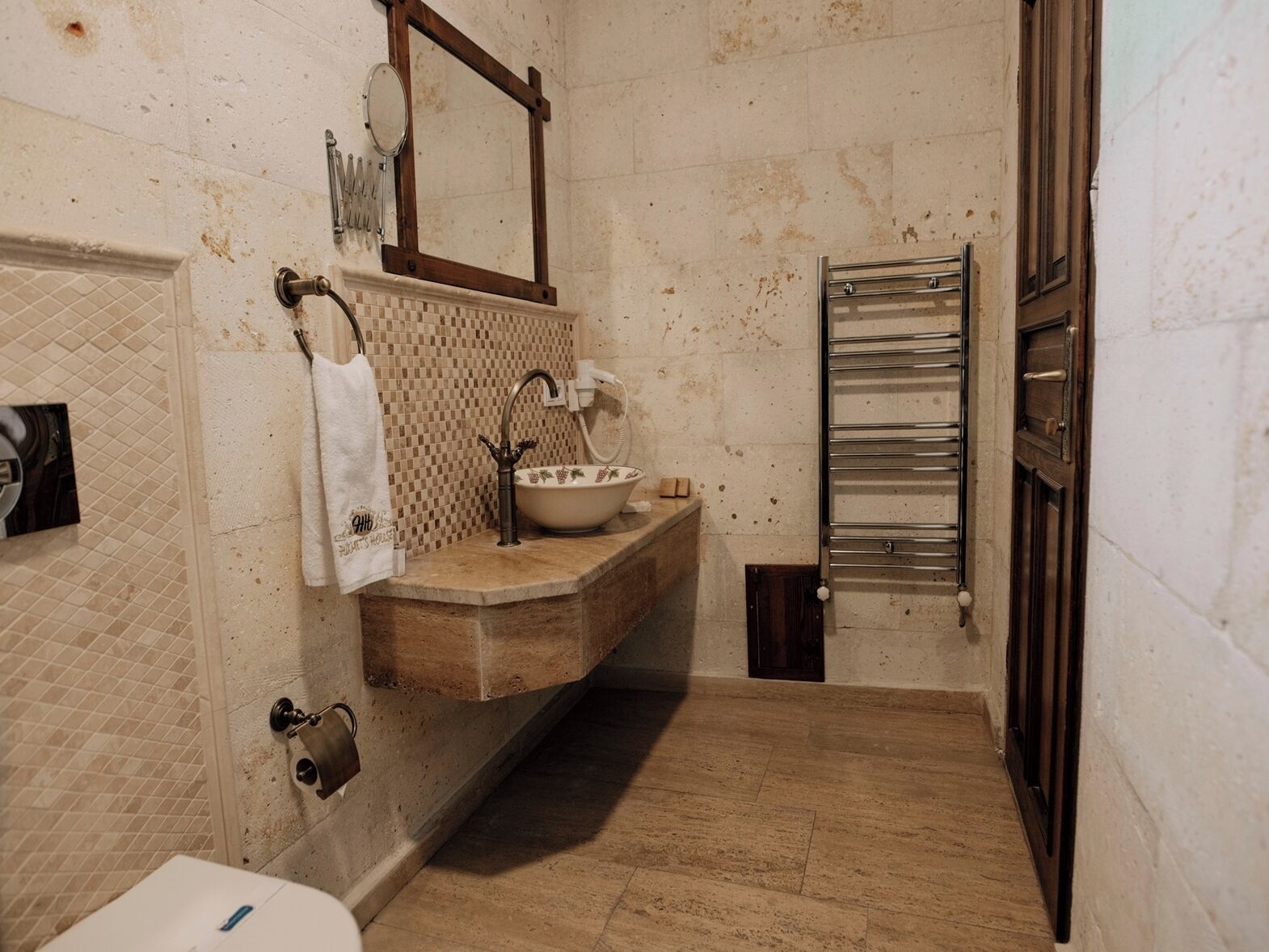 A bathroom with a tiled floor, a sink with a basin, a mirror, and a towel hanging on the wall.