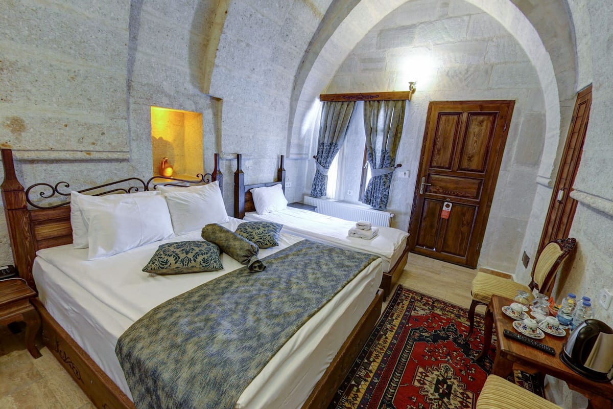 Une chambre à coucher avec un lit, une table de chevet, une lampe, une fenêtre avec des rideaux, une porte en bois et un téléviseur fixé au mur.