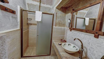 A bathroom with a glass door shower, a sink with a mosaic backsplash, and a wooden-framed mirror.