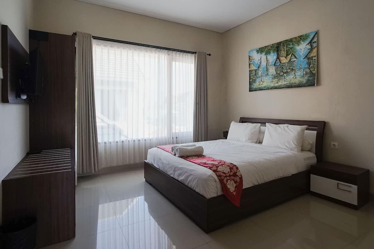 A bedroom with a bed, a nightstand, a TV, a window with curtains, and a painting on the wall.