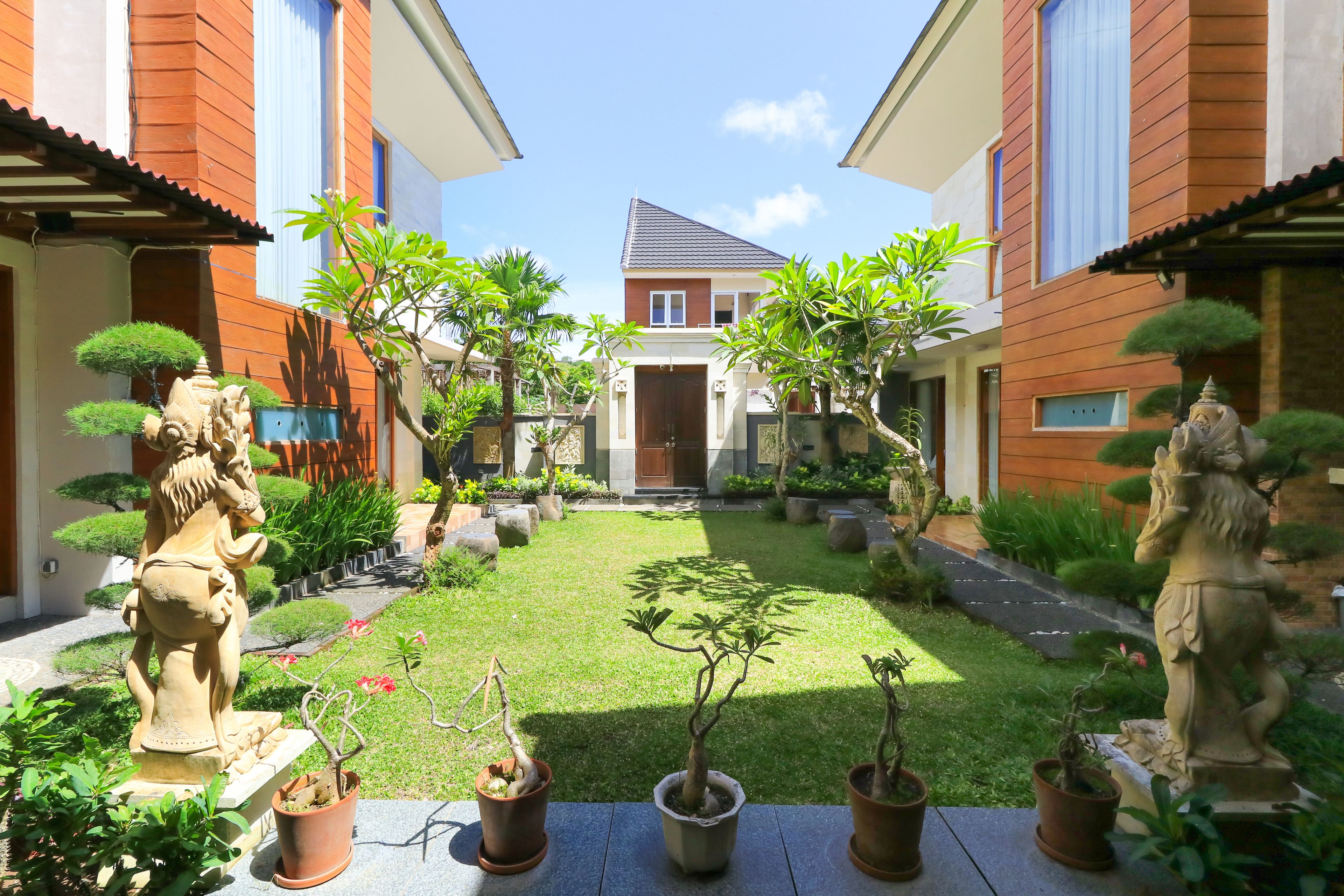 A courtyard with a central lawn, potted plants, and stone statues.