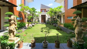 A courtyard with a central lawn, potted plants, and stone statues.
