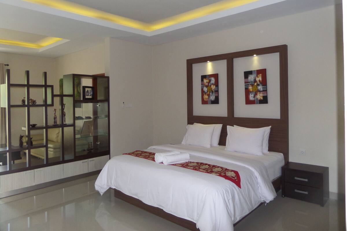 A modern hotel room with a large bed, a glass partition, and artwork on the walls.