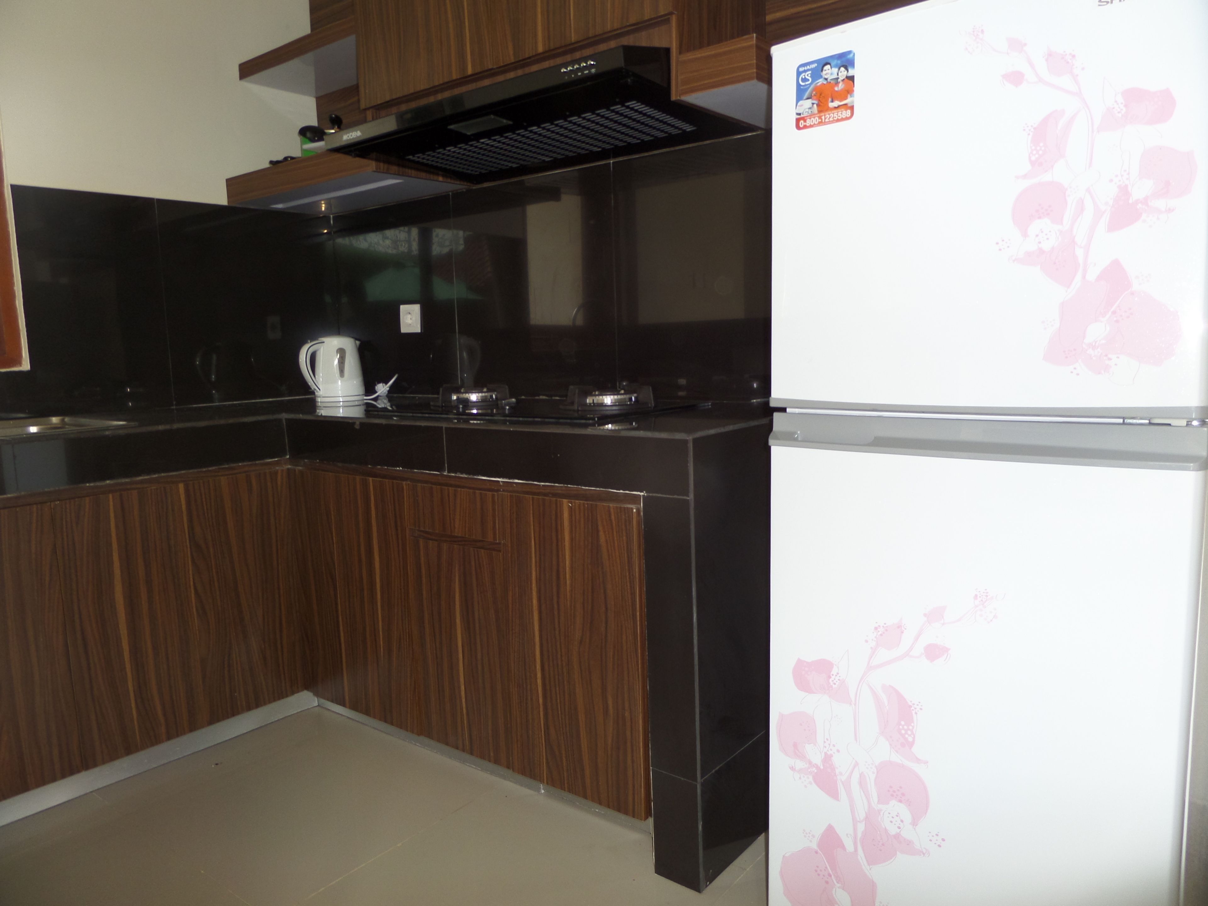 A kitchen with dark wood cabinets, a black countertop, a stainless steel range hood, and a white refrigerator with a floral decal.
