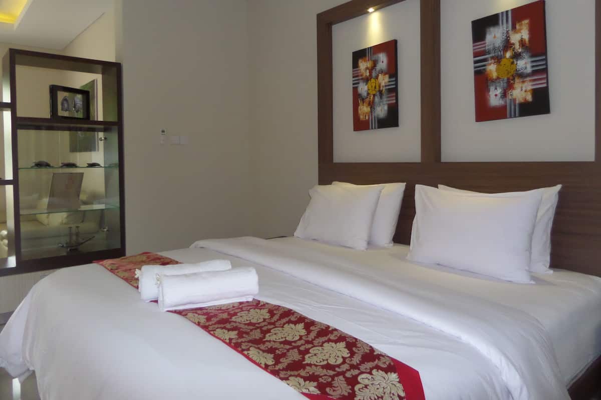 A hotel room with a neatly made bed, a glass display cabinet, and two abstract paintings on the wall.