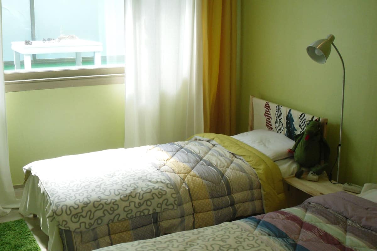 Un dormitorio con dos camas, una ventana con cortinas, una lámpara y una pared verde.