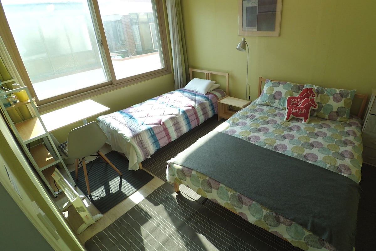 Habitación tipo dormitorio con dos camas, un escritorio, una silla, una mesita, una lámpara y un archivador.