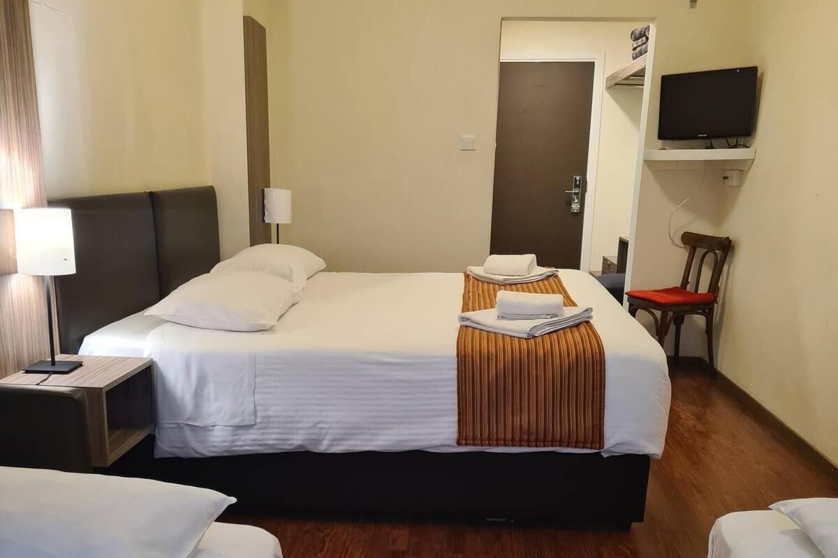 A hotel room with a large bed, a smaller bed, a TV, a chair, and a wooden floor.