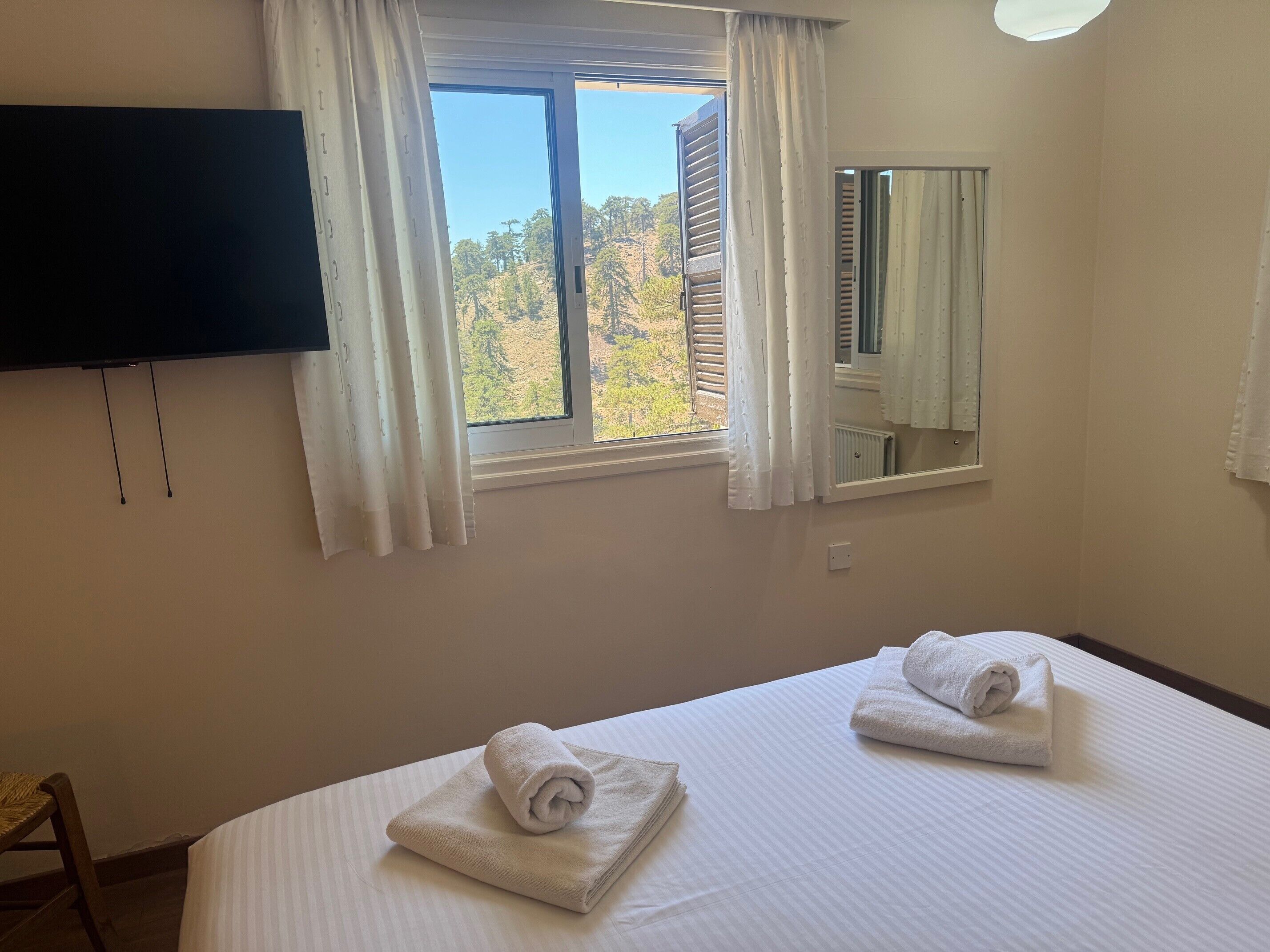 Habitación de hotel con dos camas, un televisor montado en la pared, una ventana con cortinas y un espejo.