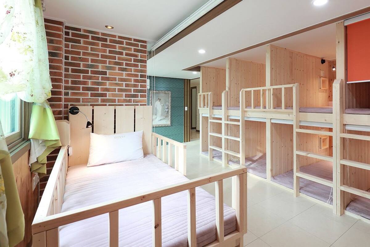 A room with bunk beds, a window with curtains, a brick wall, and a wooden partition.