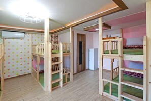 A room with bunk beds, a wooden floor, a white air conditioner, and a door leading to another room.