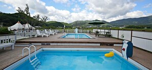A pool area with two pools, deck chairs, and a view of mountains. - Favian Guest House (Gyeongju)