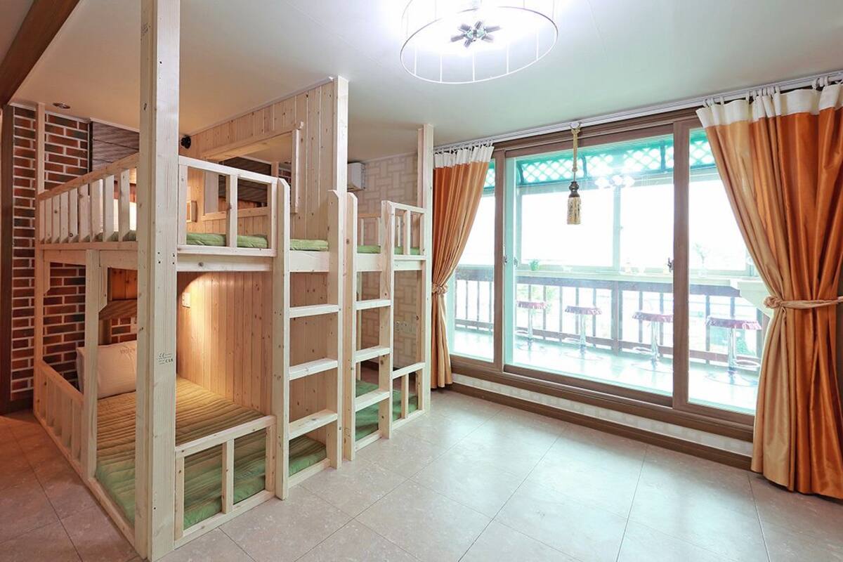 A room with bunk beds, a large window with curtains, and a view of an outdoor deck.