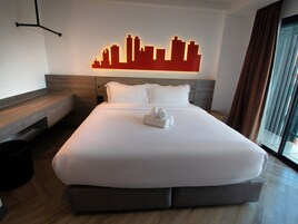 Habitación de hotel con una cama grande, un cuadro de un horizonte urbano, un banco de madera y un ventanal con cortinas.
