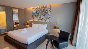 A modern hotel room with a large bed, a small table, a chair, and a wall art piece. - Fortune D Hotel Phitsanulok (Phitsanulok)