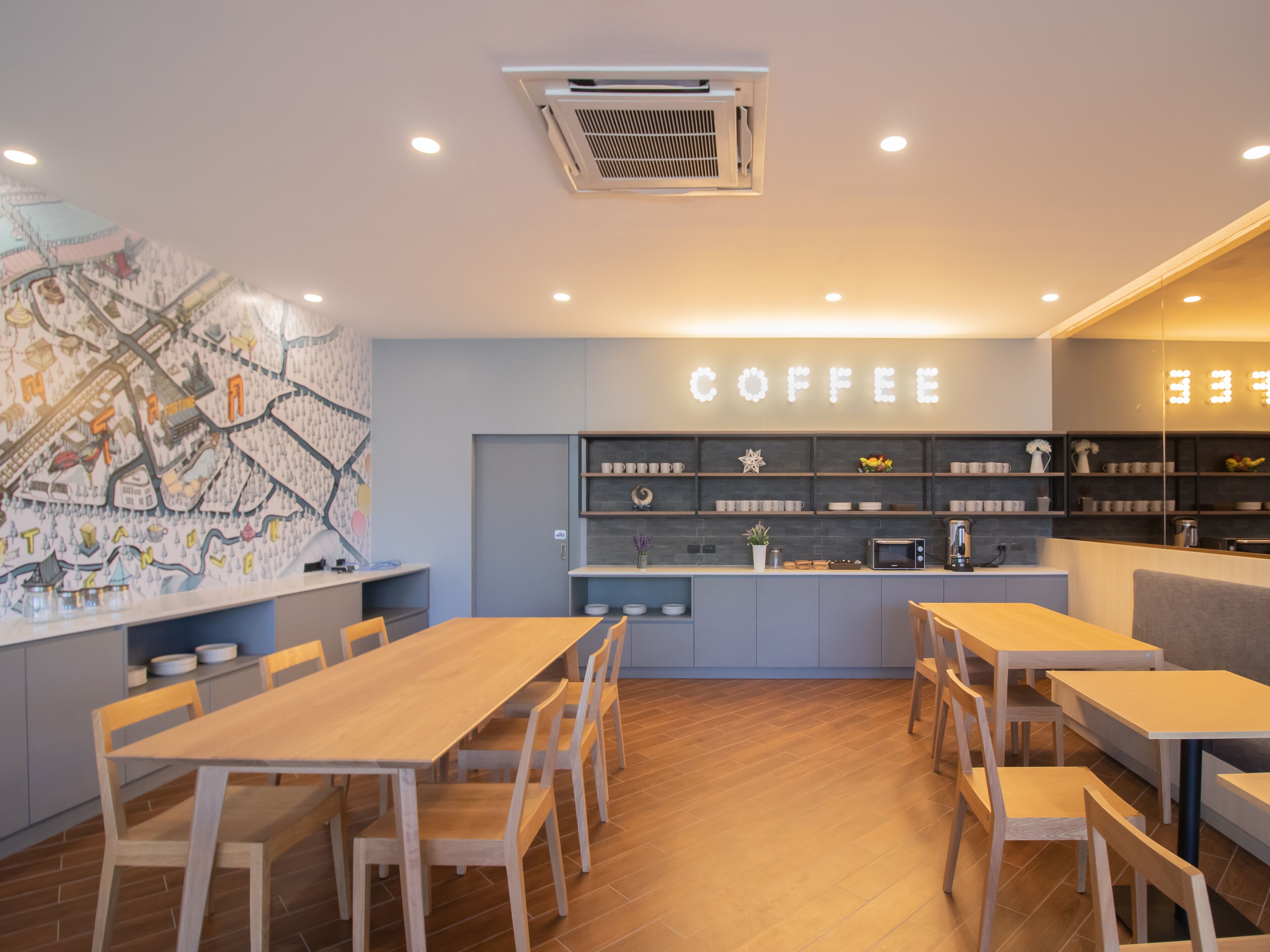 A modern coffee shop with wooden tables and chairs, a wall-mounted coffee machine, and a large illuminated sign that reads "COFFEE".