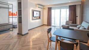 A modern hotel room with a bed, a TV mounted on the wall, a dining area with a table and chairs, and a balcony with curtains. - Fortune D Hotel Phitsanulok (Phitsanulok)