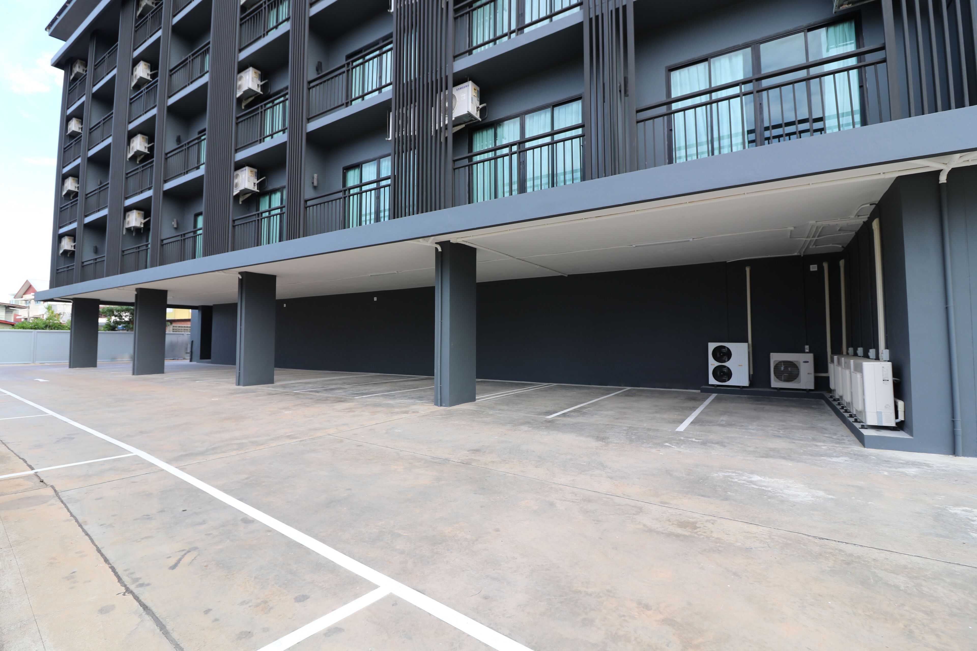 Un edificio moderno con estacionamiento techado, unidades de aire acondicionado y un piso de concreto impecable.
