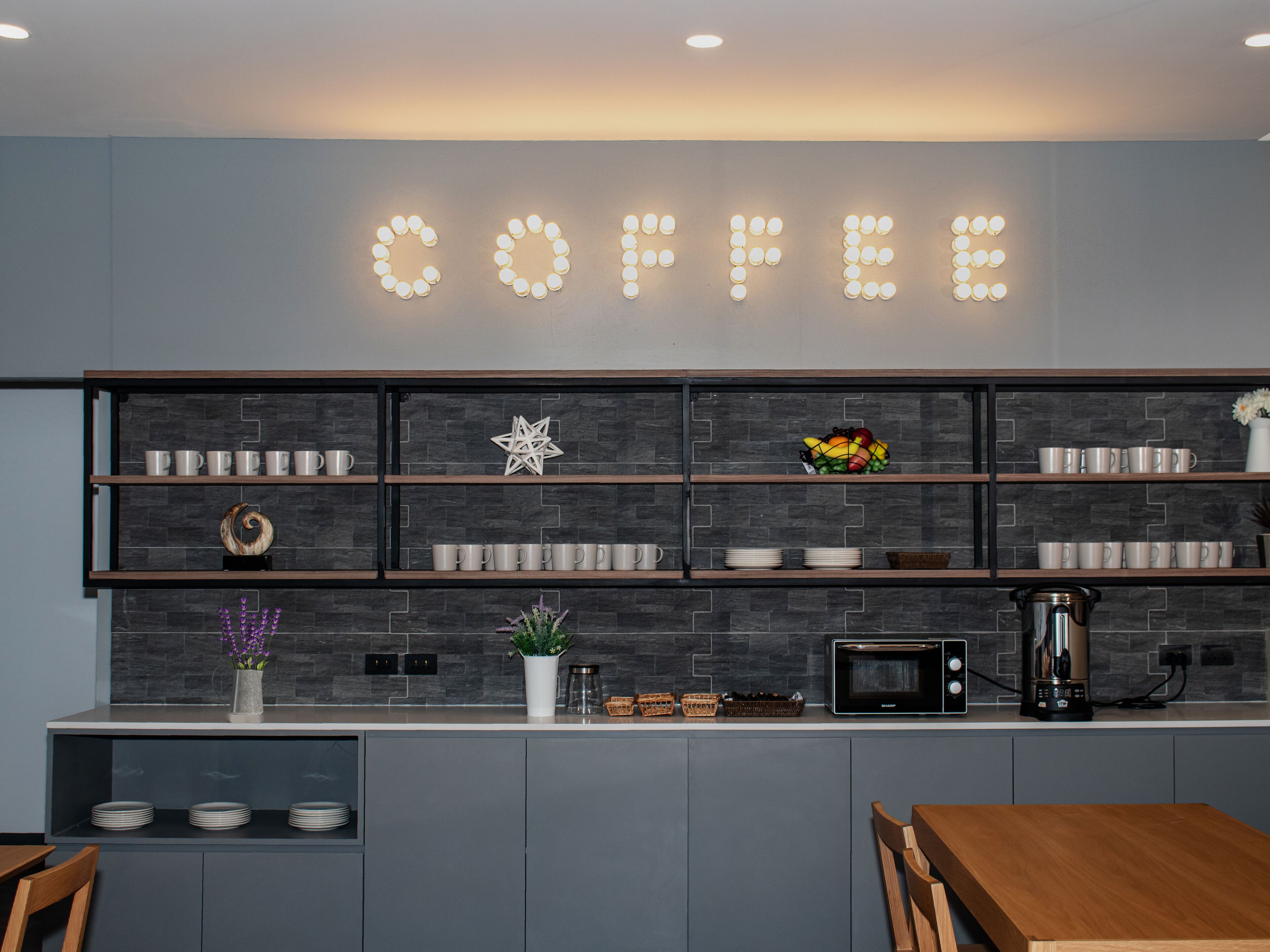 A modern kitchen with a 'COFFEE' sign, shelves with mugs, a star decoration, and a fruit bowl.