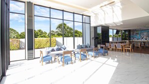 A spacious indoor area with large windows, a seating area with sofas and chairs, and a dining area with tables and chairs. - Fortune D Hotel Phitsanulok (Phitsanulok)