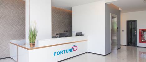 Un mostrador de recepción con el logotipo 'FORTUNE', una planta en maceta y un diseño de interiores moderno.