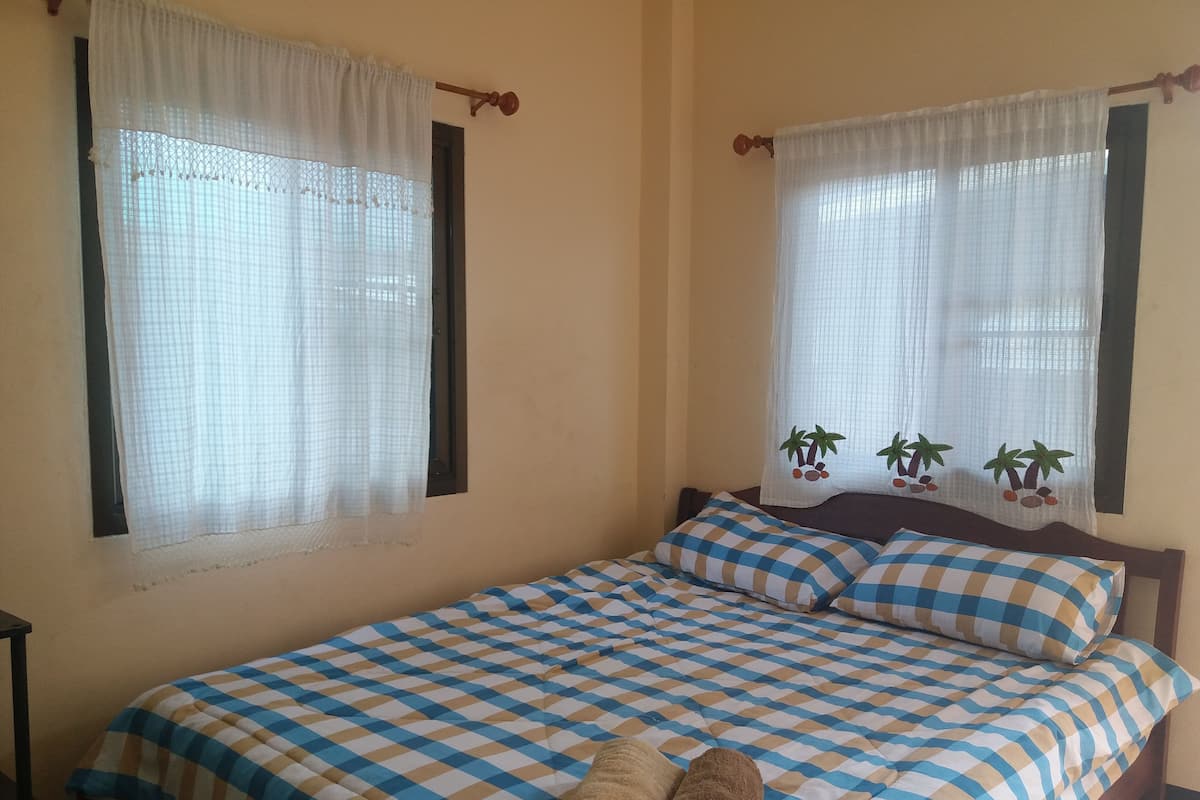 A bed with a checkered bedspread, two pillows, and two rolled towels.