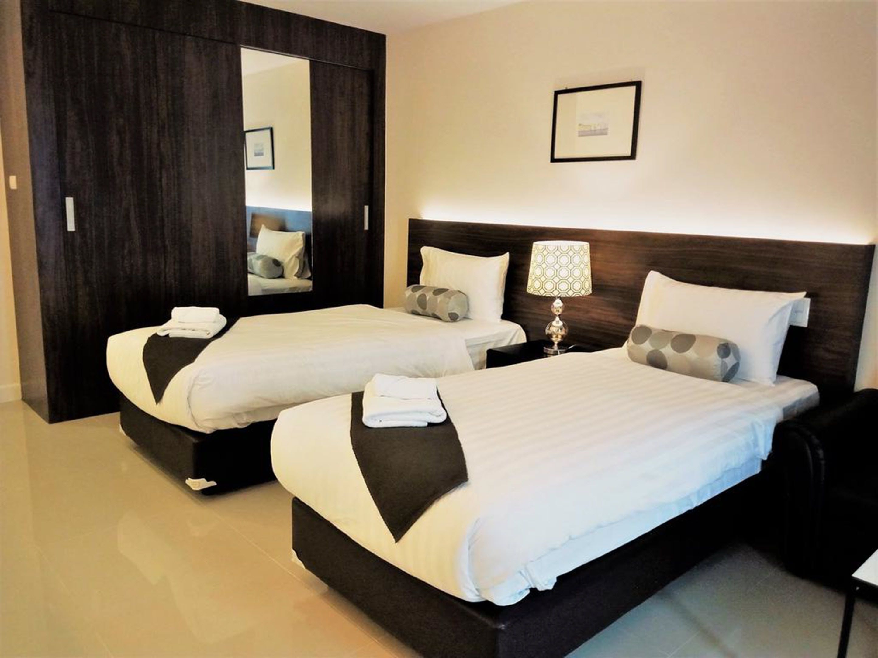 Habitación de hotel con dos camas, cabeceros de madera oscura, un espejo grande y un cuadro en la pared.